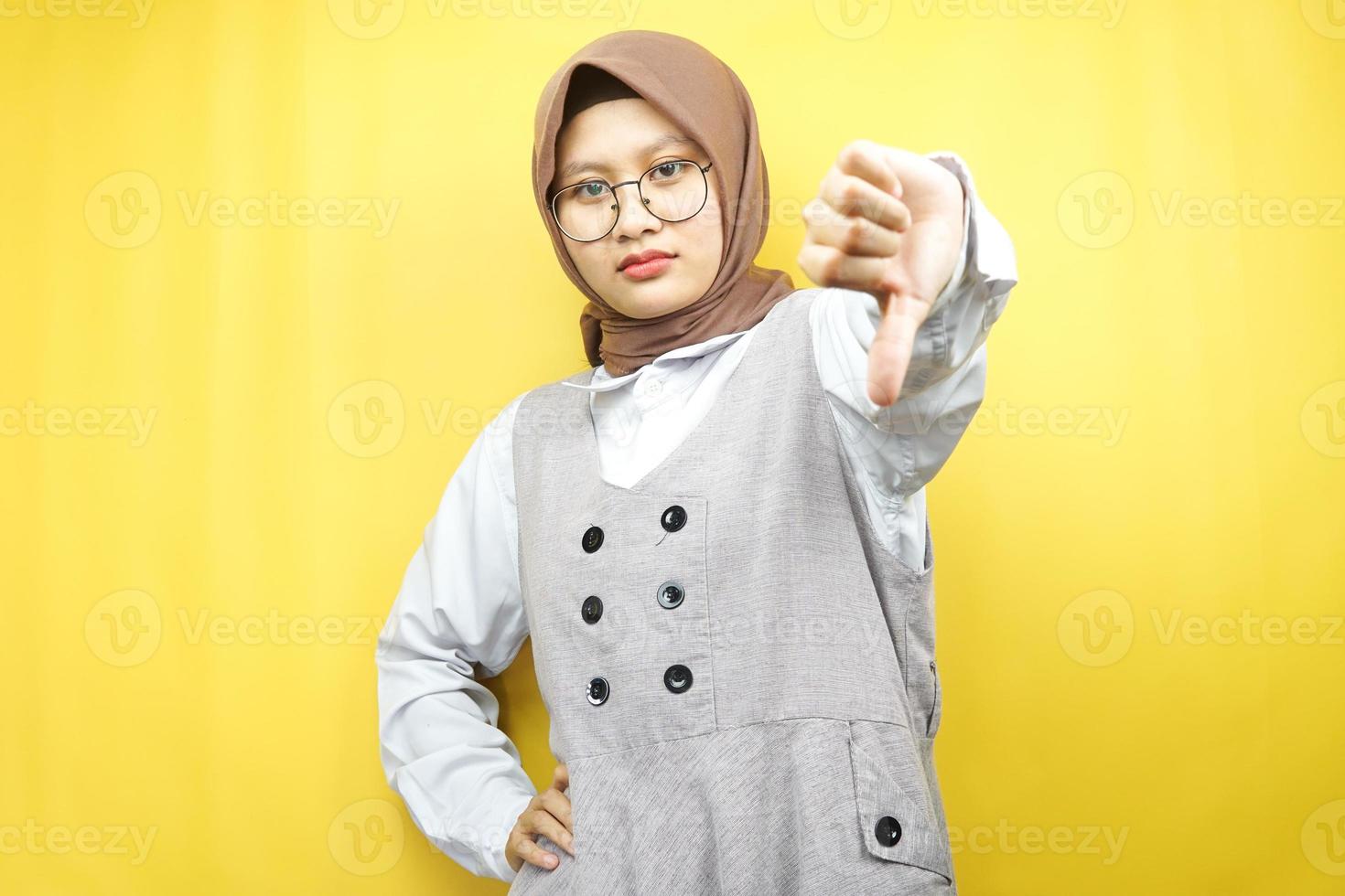 Beautiful young asian muslim woman dislike, belittling, disappointed, dissatisfied, not good, bad job, lousy, weak, looking at camera isolated on yellow background photo