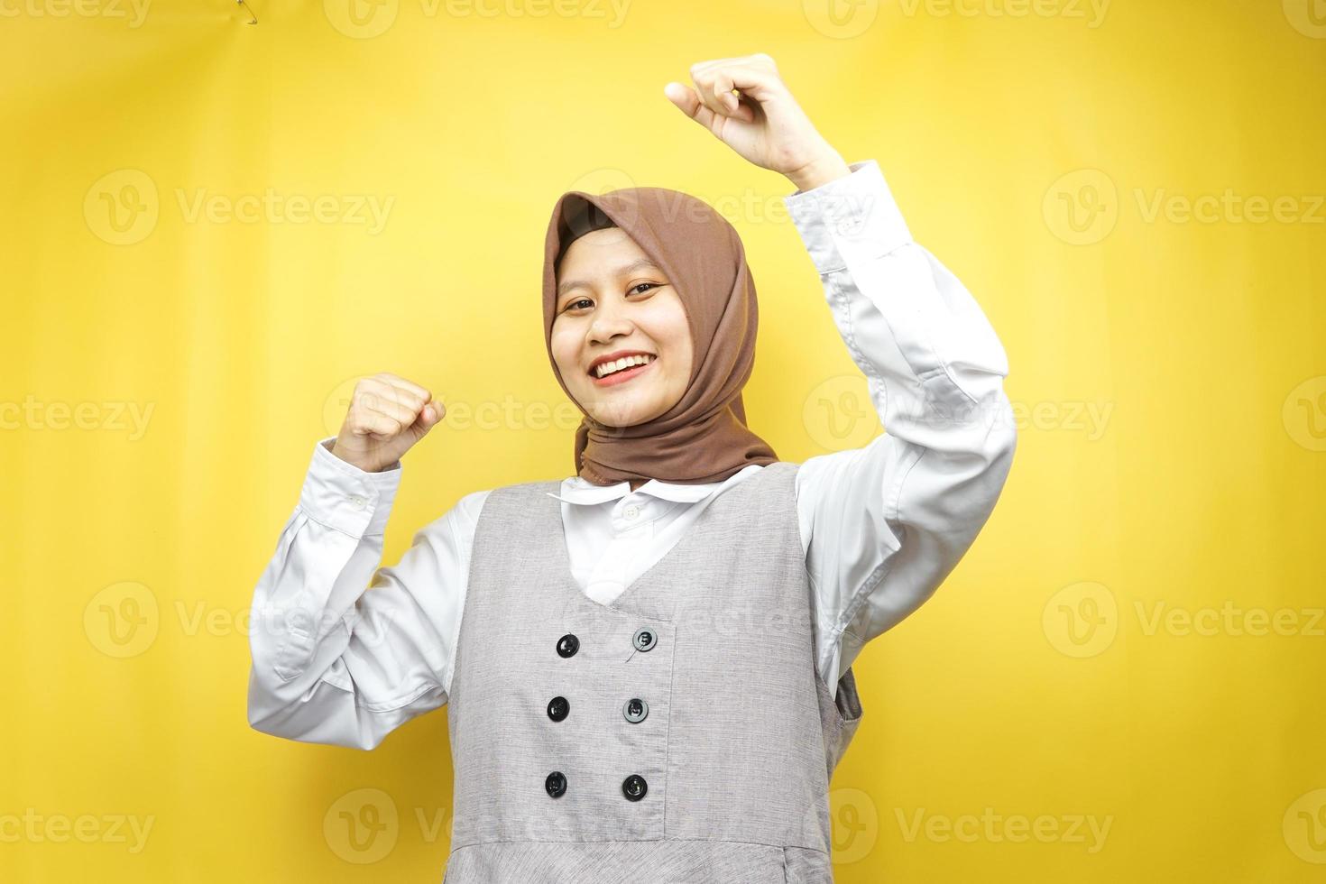 Beautiful young asian muslim woman smiling confident, enthusiastic and cheerful with  hands clenched, sign of success, punching, fighting, not afraid, isolated on yellow background photo