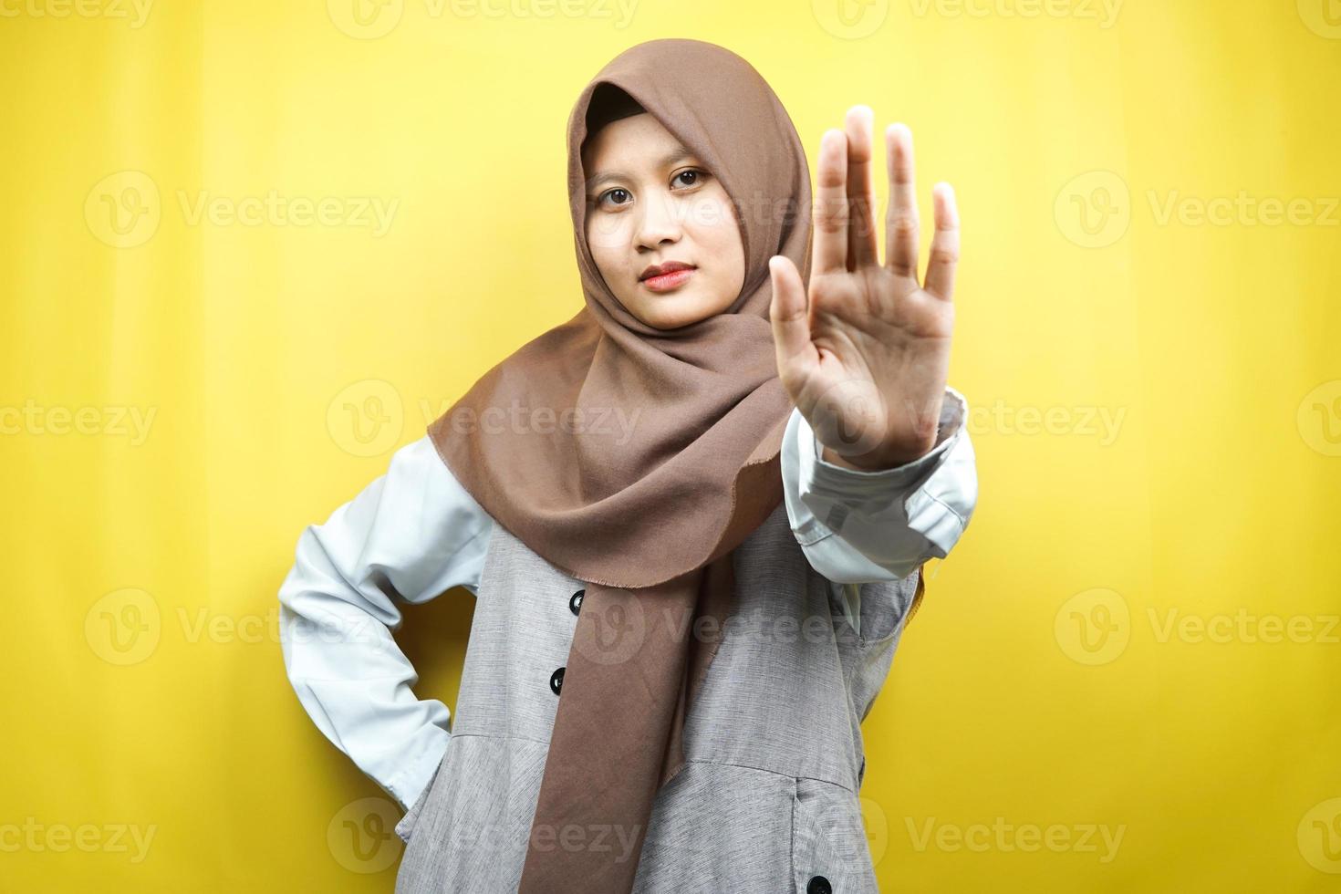 Hermosa mujer musulmana joven asiática con la mano de la señal de pare, rechazar la mano de la señal, mano de la señal de prohibición, no acercarse a la mano, mantenerse alejado de la mano del signo, no mover la mano del signo, aislado sobre fondo amarillo foto