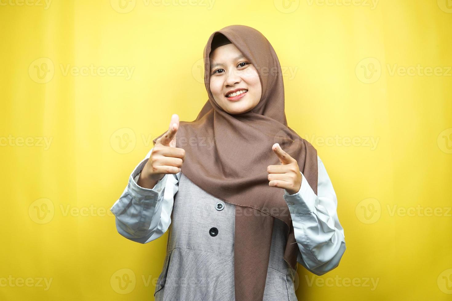 Hermosa joven musulmana asiática sonriendo confiada, entusiasta y alegre con las manos apuntando a la cámara, las manos apuntando a la audiencia, frente a la cámara aislada sobre fondo amarillo foto