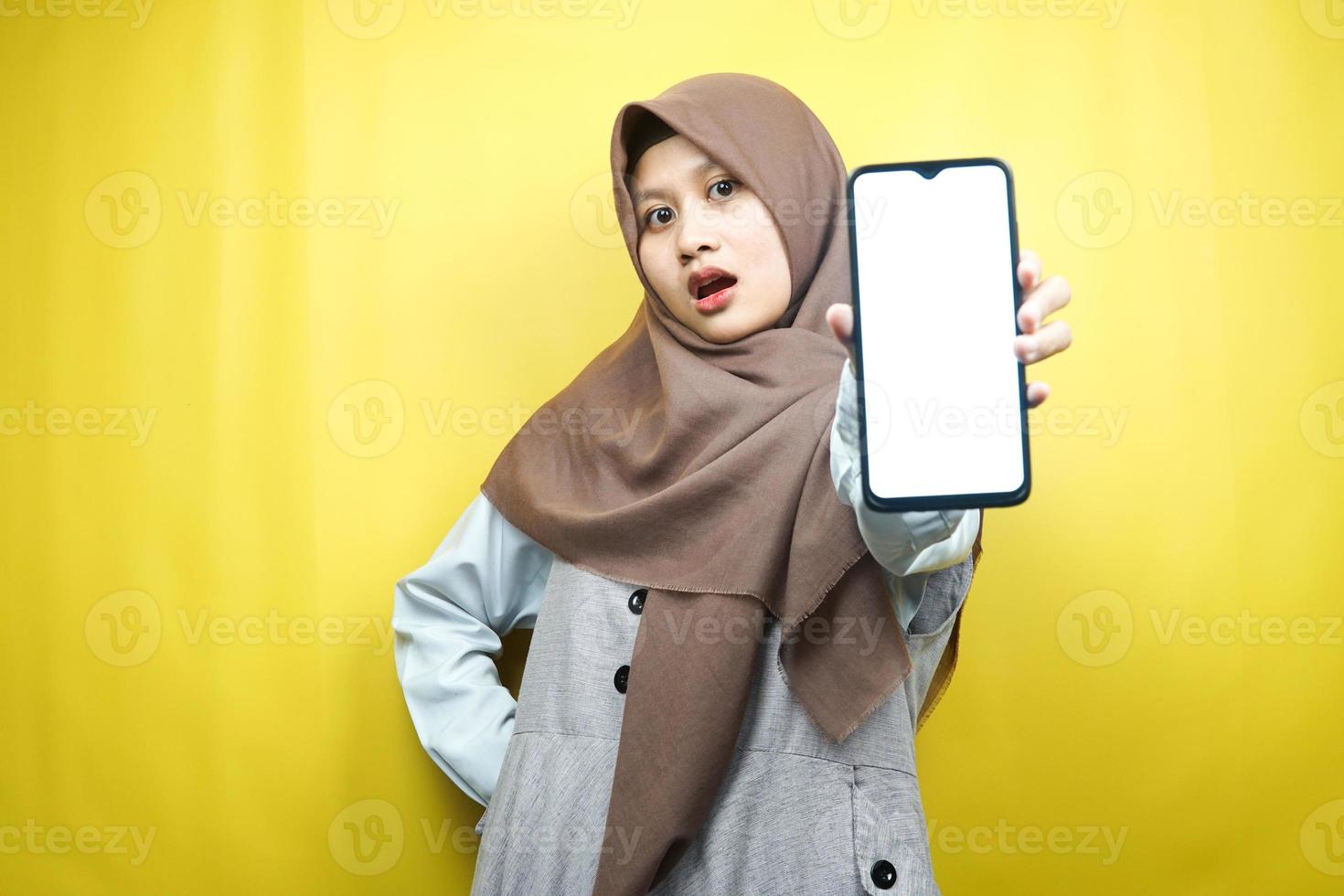 Hermosa joven mujer musulmana asiática conmocionada, sorprendida, expresión guau, mano sosteniendo un teléfono inteligente con pantalla blanca o en blanco, promocionando la aplicación, promocionando el producto, presentando algo, aislado foto