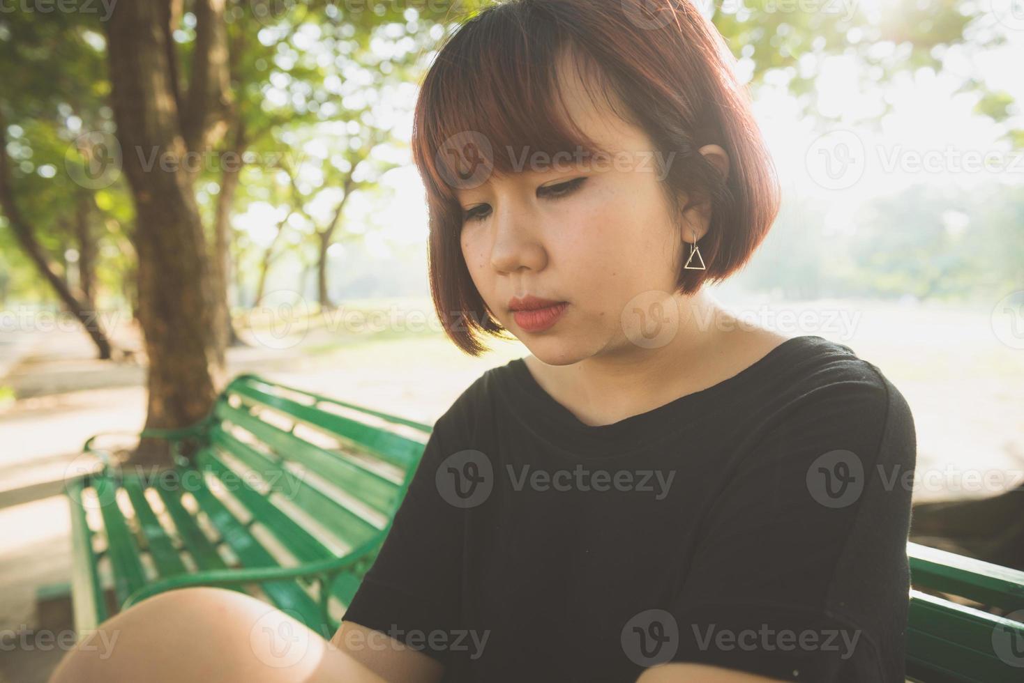 joven asiática sentada al aire libre en el banco público y acostada a lo largo del banco en el parque en un cálido día de luz solar. mujer joven relajar su mente y cuerpo en el parque. actividad al aire libre en el concepto de parque. foto