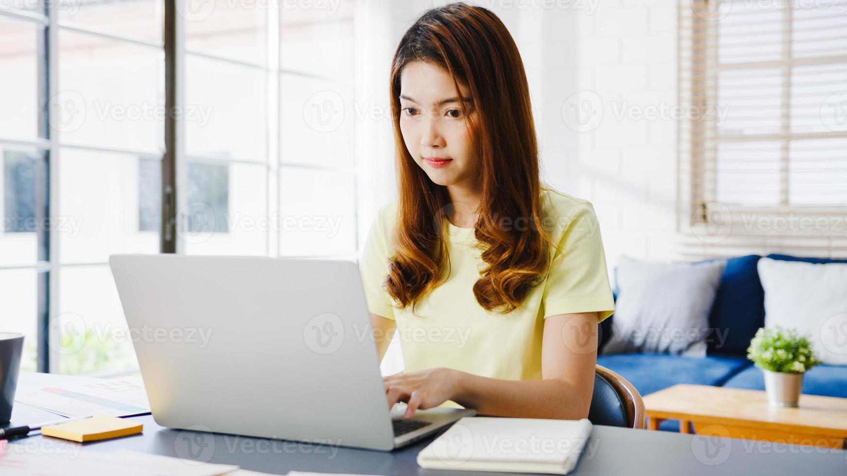 Portrait of freelance Asia women casual wear using laptop working in living room at home. Working from home, remotely work, self isolation, social distancing, quarantine for corona virus prevention. photo