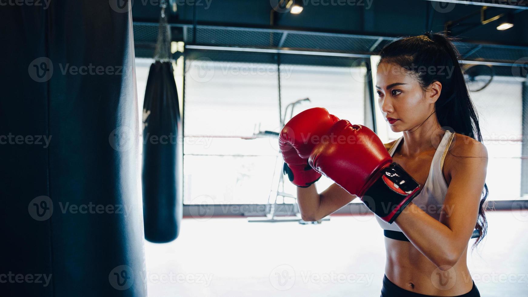 Young Asia lady kickboxing exercise workout punching bag tough female fighter practice boxing in gym fitness class. Sportswoman recreational activity, functional training, healthy lifestyle concept. photo