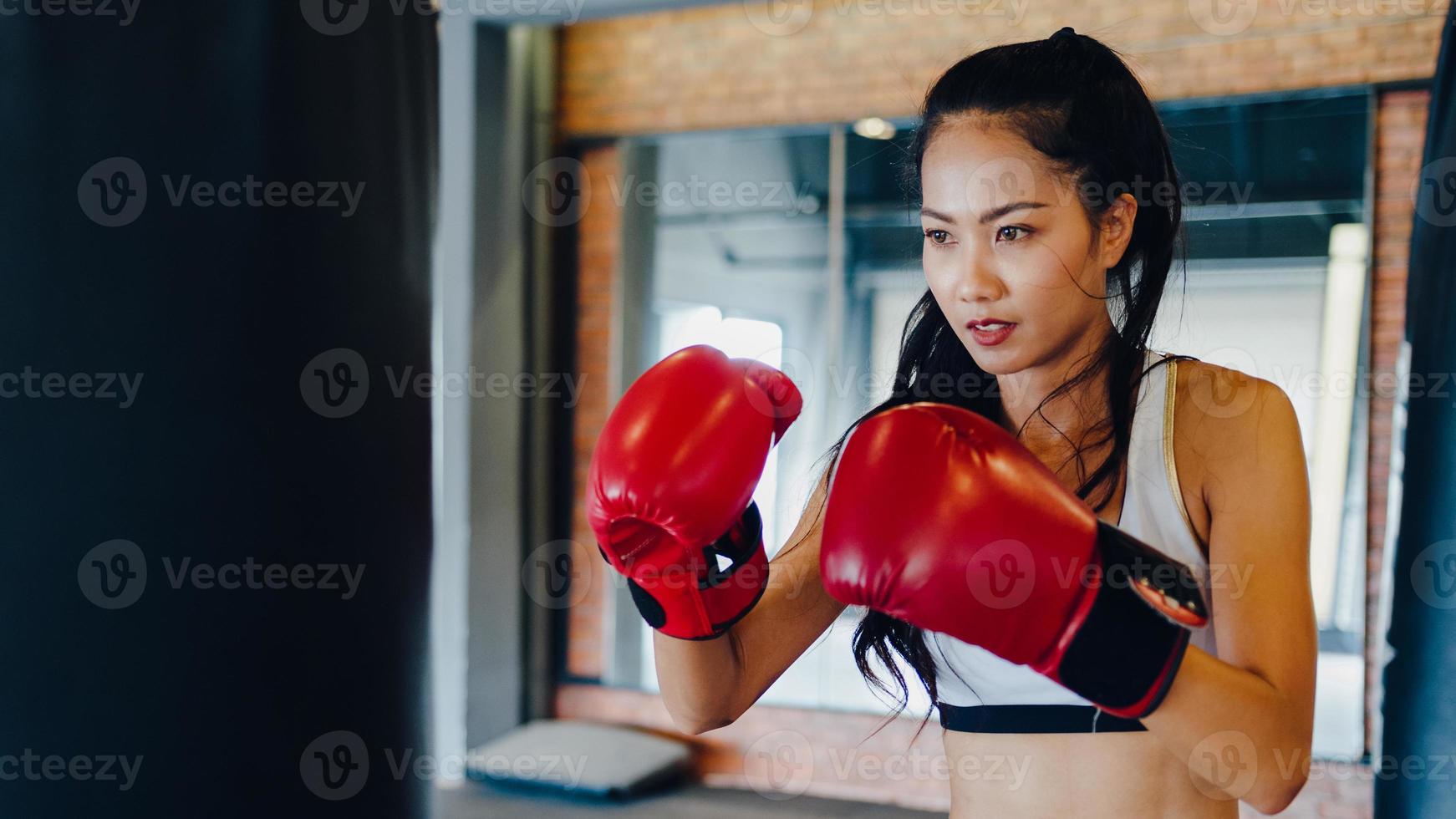 Young Asia lady kickboxing exercise workout punching bag tough female fighter practice boxing in gym fitness class. Sportswoman recreational activity, functional training, healthy lifestyle concept. photo