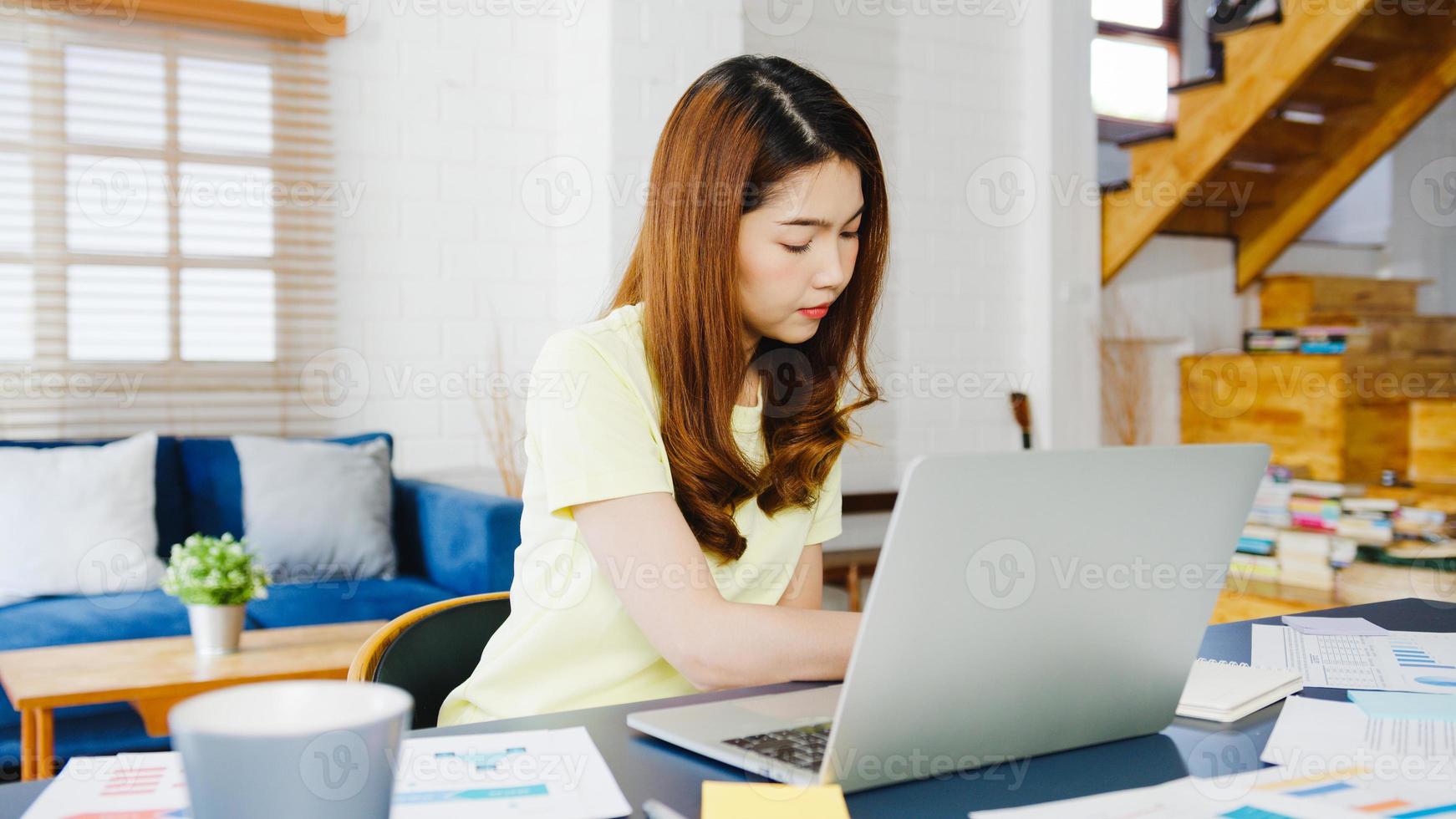 Retrato de ropa casual de mujeres asiáticas independientes usando una computadora portátil que trabaja en la sala de estar en casa. trabajo desde casa, trabajo a distancia, autoaislamiento, distanciamiento social, cuarentena para la prevención del coronavirus. foto