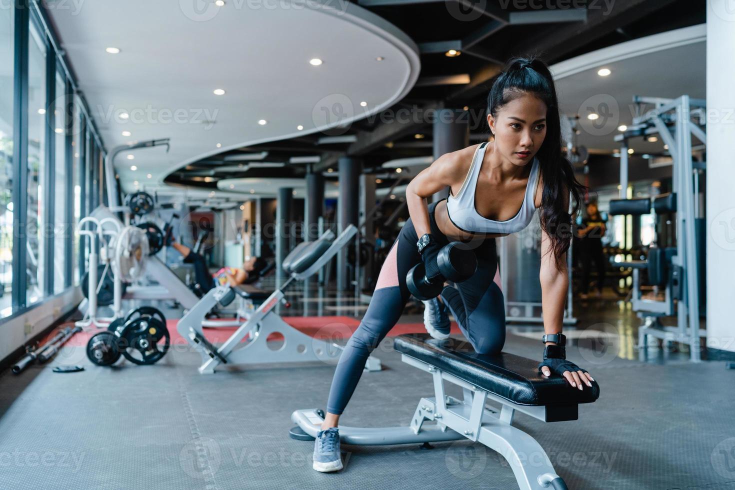 Hermosa joven asiática ejercicio haciendo ejercicio para quemar grasa con barra de elevación en la clase de gimnasia. atleta con six pack, actividad recreativa deportista, entrenamiento funcional, concepto de estilo de vida saludable. foto