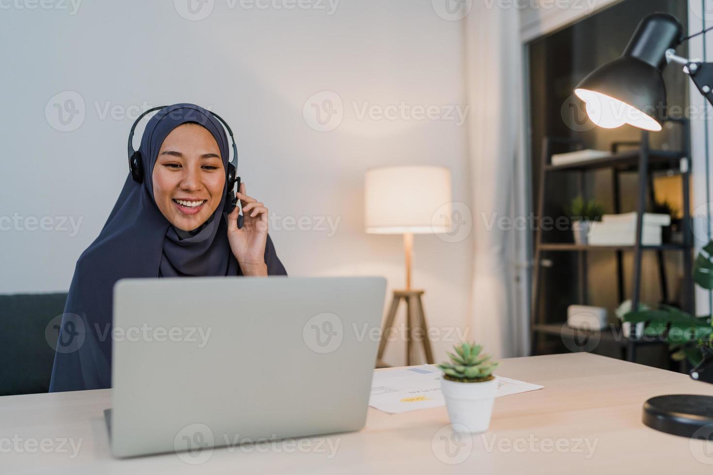 Asia dama musulmana usar audífonos ver seminario web escuchar curso en línea comunicarse por videoconferencia en la oficina en casa de noche. trabajo a distancia desde casa, distancia social, cuarentena para virus corona. foto