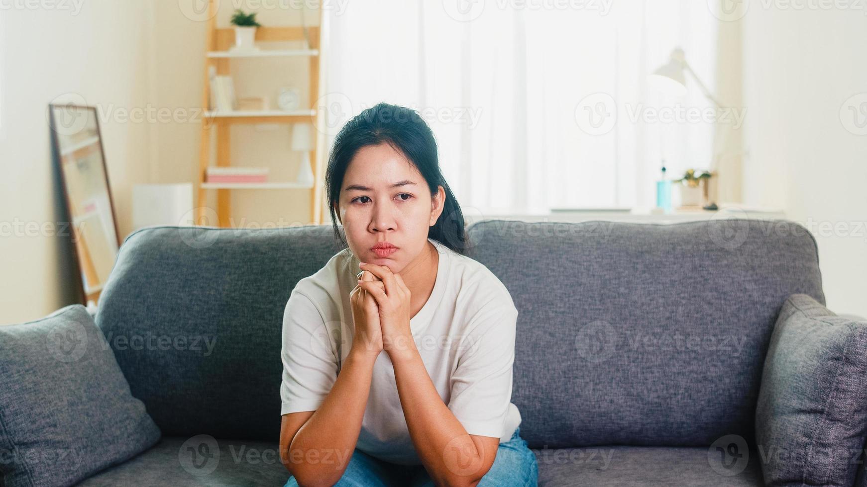 Mujer de negocios asiática llorando deprimida estresada con dolor de cabeza sentada en el sofá en la sala de estar de la casa cuando el distanciamiento social se queda en casa y el tiempo de auto cuarentena, concepto de coronavirus. foto