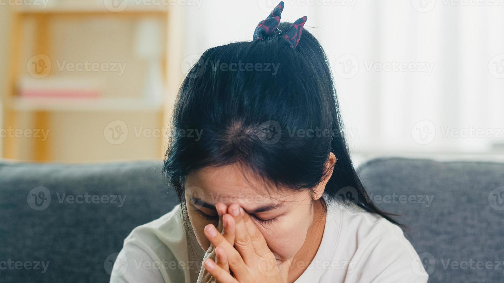 Depressed crying Asian business woman stressed with headache sitting on sofa in living room at house when social distancing stay at home and self quarantine time, coronavirus concept. photo