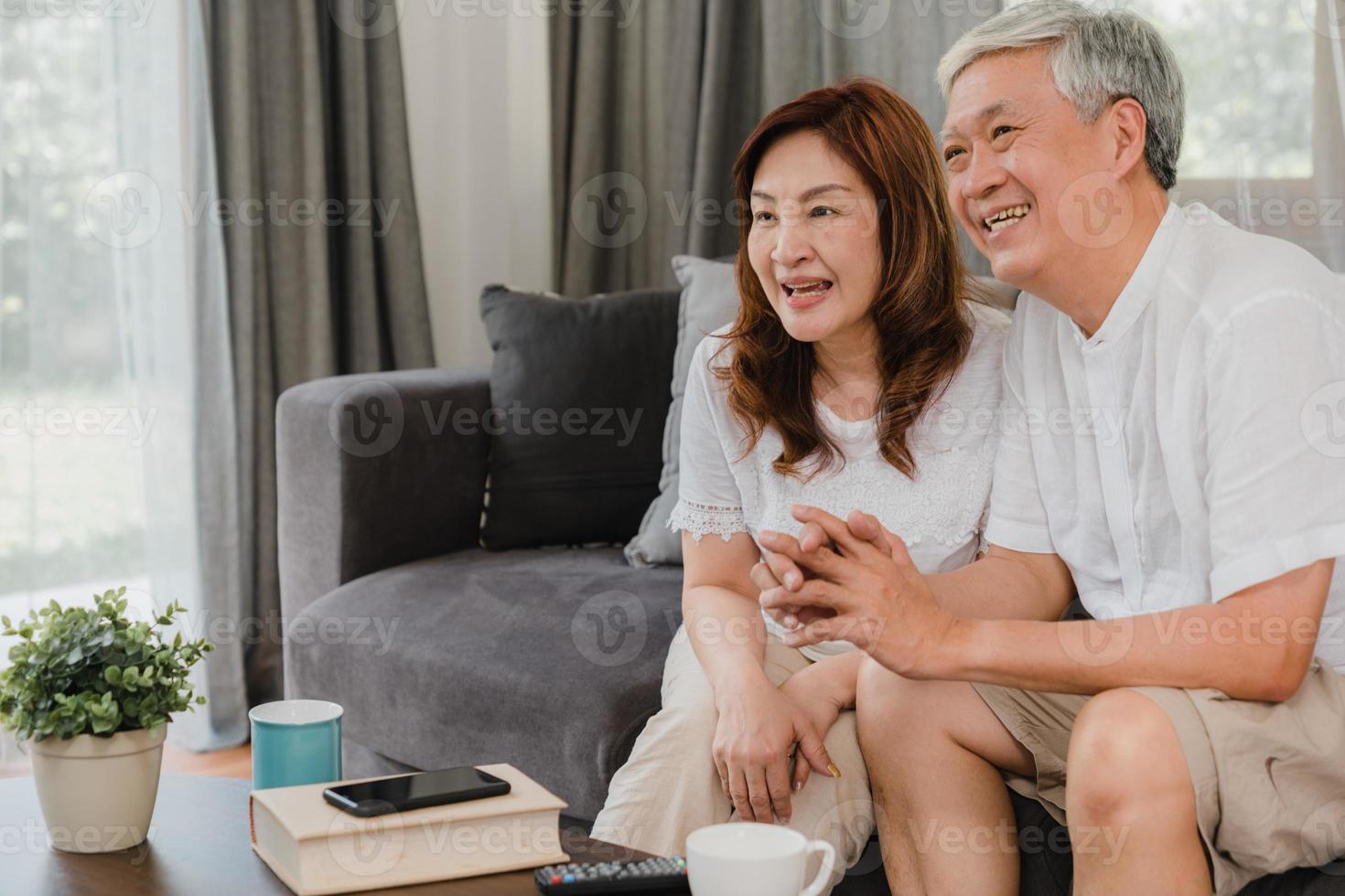 Pareja de ancianos asiáticos viendo la televisión en la sala de estar en casa, la dulce pareja disfruta de un momento de amor mientras está acostada en el sofá cuando está relajada en casa. disfrutando del tiempo de estilo de vida de la familia senior en el concepto de hogar. foto