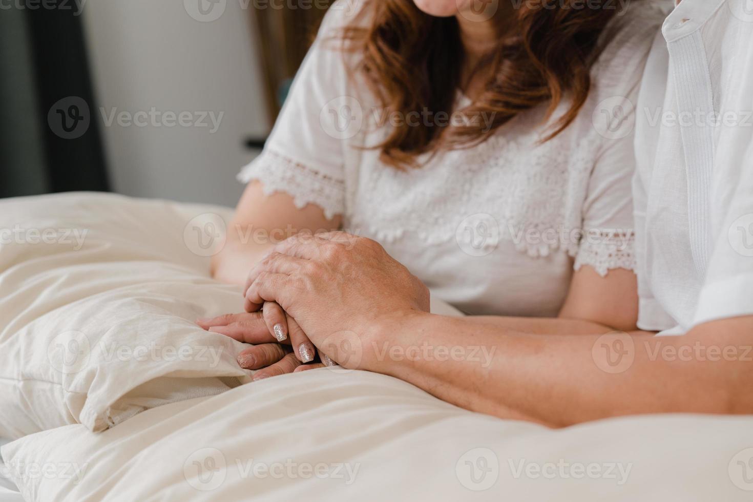 pareja de ancianos asiáticos tomados de la mano mientras se toman juntos en el dormitorio, la pareja se siente feliz comparte y se apoya mutuamente acostados en la cama en casa. familia senior de estilo de vida en el concepto de hogar. foto