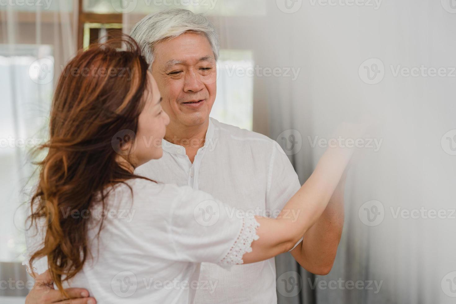 Pareja de ancianos asiáticos bailando juntos mientras escuchan música en la sala de estar en casa, la dulce pareja disfruta del momento de amor mientras se divierte cuando está relajada en casa. familia senior de estilo de vida relajarse en el concepto de hogar. foto