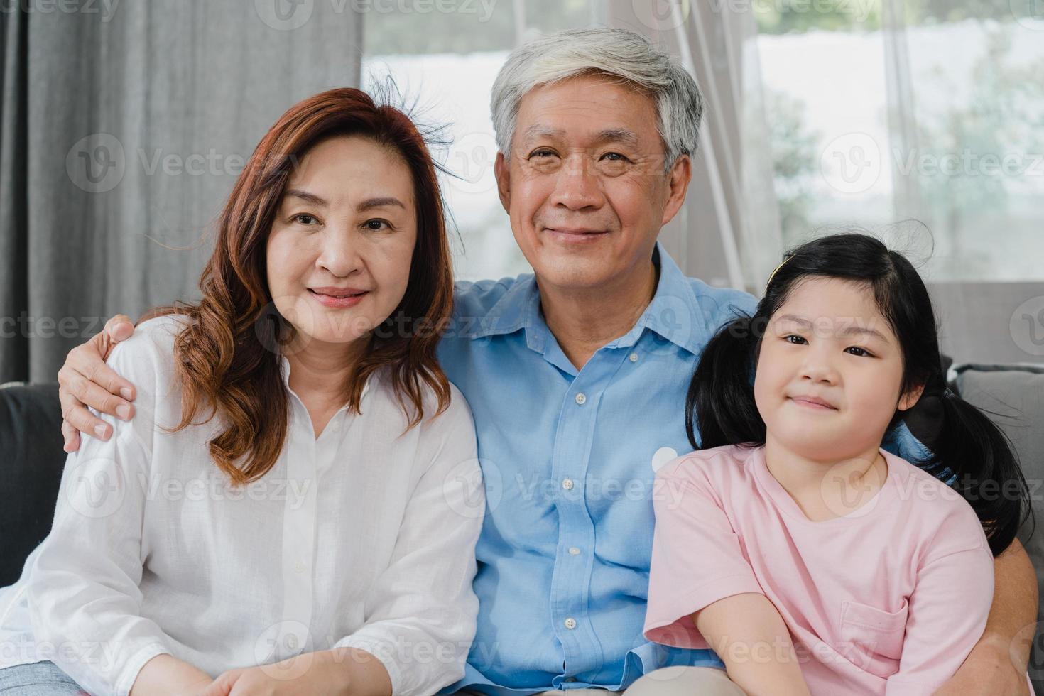 los abuelos asiáticos ven la televisión con su nieta en casa. chino senior, abuelo y abuela felices usando tiempo en familia relajarse con un niño niña acostado en el sofá en el concepto de sala de estar. foto