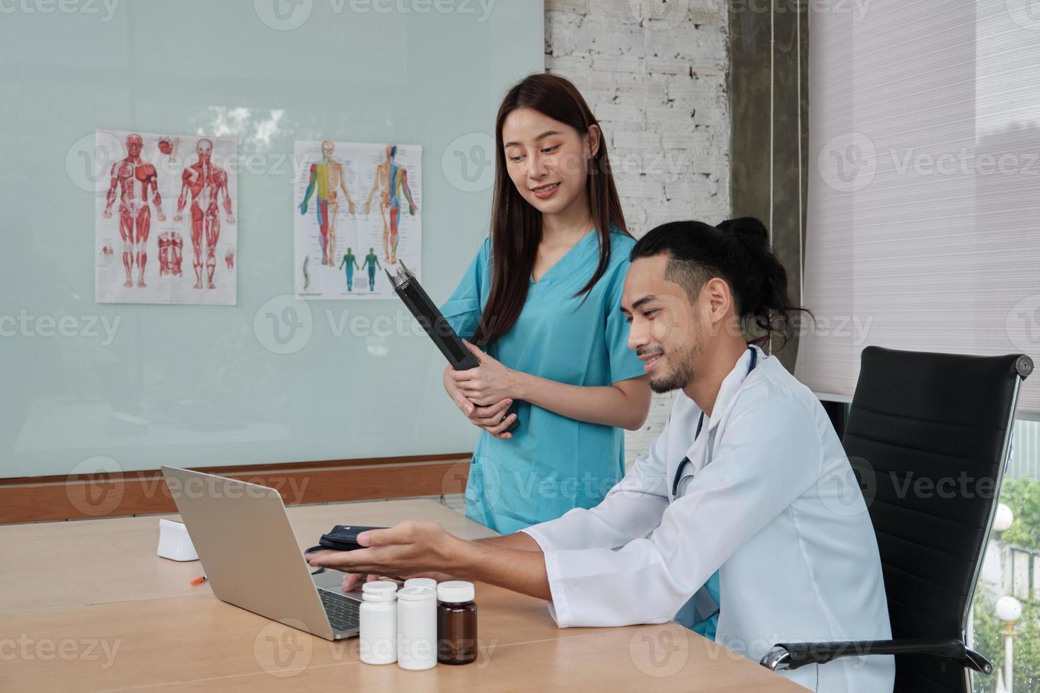 Healthcare team partners. Two uniformed young Asian ethnicity doctors are co-workers discussing medication in hospital's clinic office. Specialist persons are experts and professionals. photo