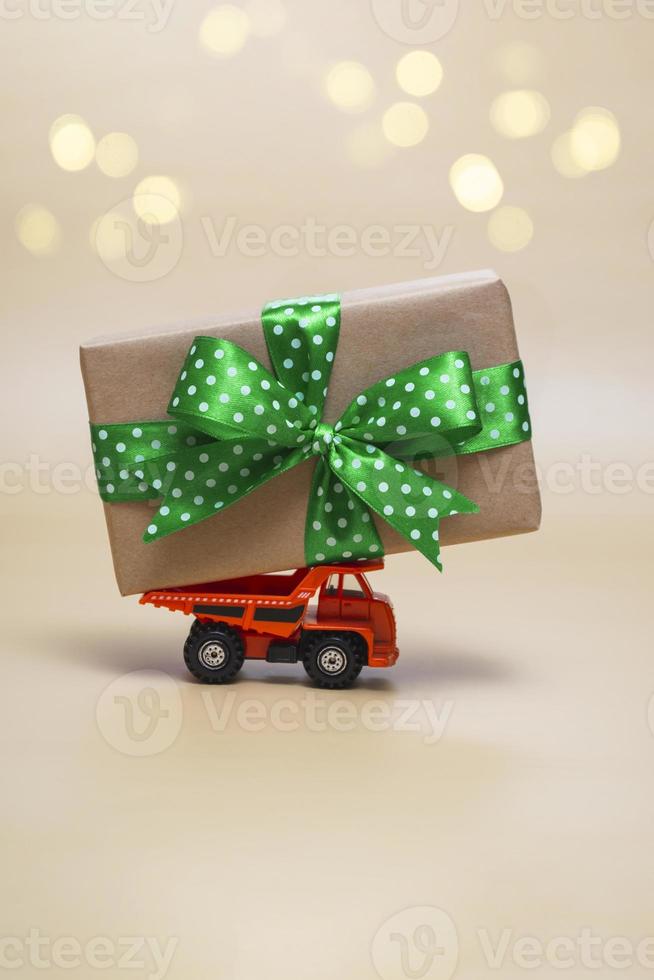 Orange truck with a large gift on a beige background. Holidays concept. Close up, with copy space. Vertical photo. photo