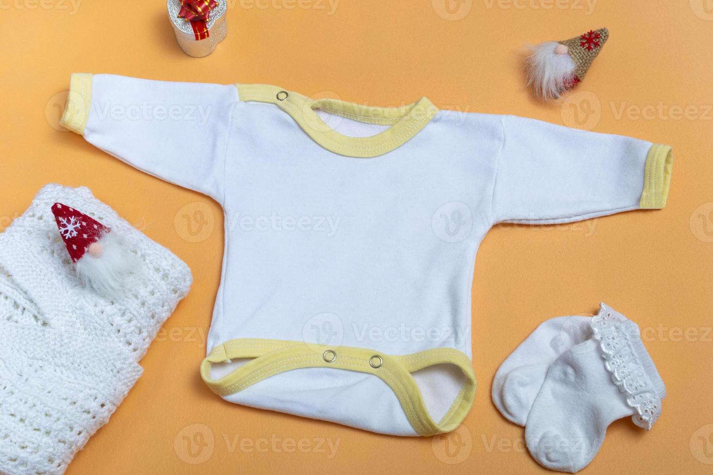 Mockup of a white baby bodysuit on a colored background close-up with a knitted white jacket and gnomes mockup of clothes for newborns. With copy space photo