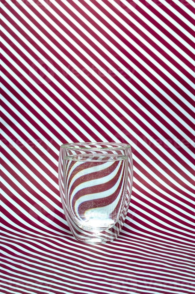 A glass of water with a double bottom on a striped background. Abstract refraction of red and white diagonals in glass. Vertical format photo