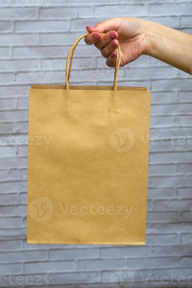 Simulacros de primer plano de envases ecológicos sobre un fondo gris ladrillo. bolsa de kraft en mano de mujer. concepto de compra online, entrega, pedidos online. foto