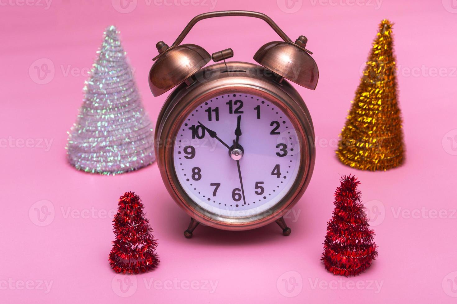 Christmas or New Years minimal concept. Alarm clock and multicolored Christmas trees on a pink background. photo