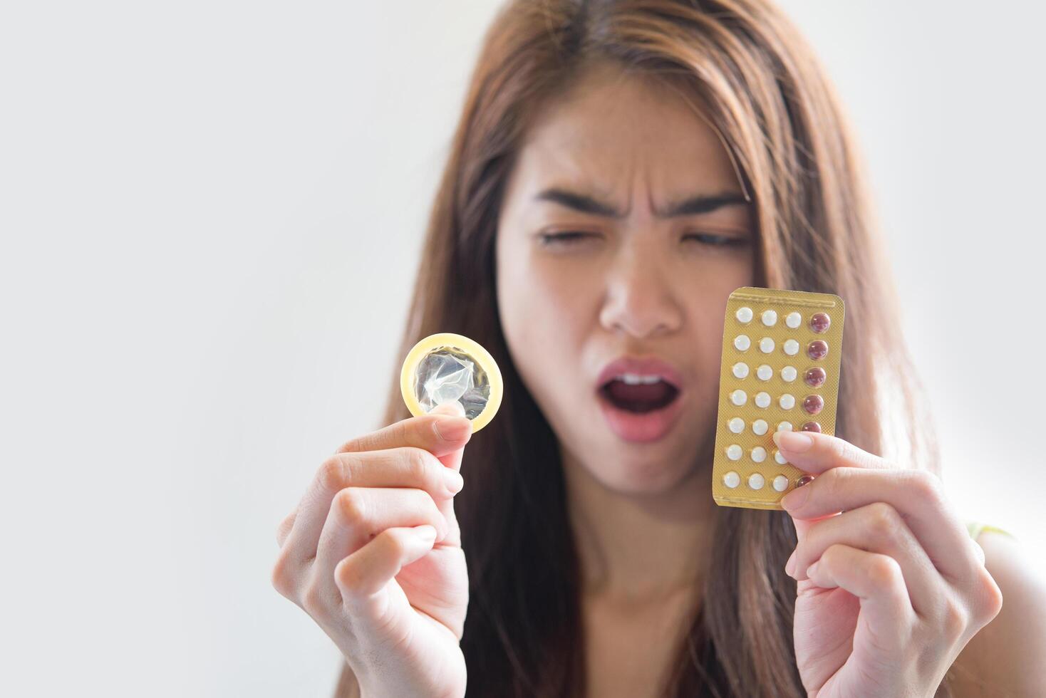 Mujer joven sosteniendo condones y píldoras anticonceptivas previenen el embarazo foto