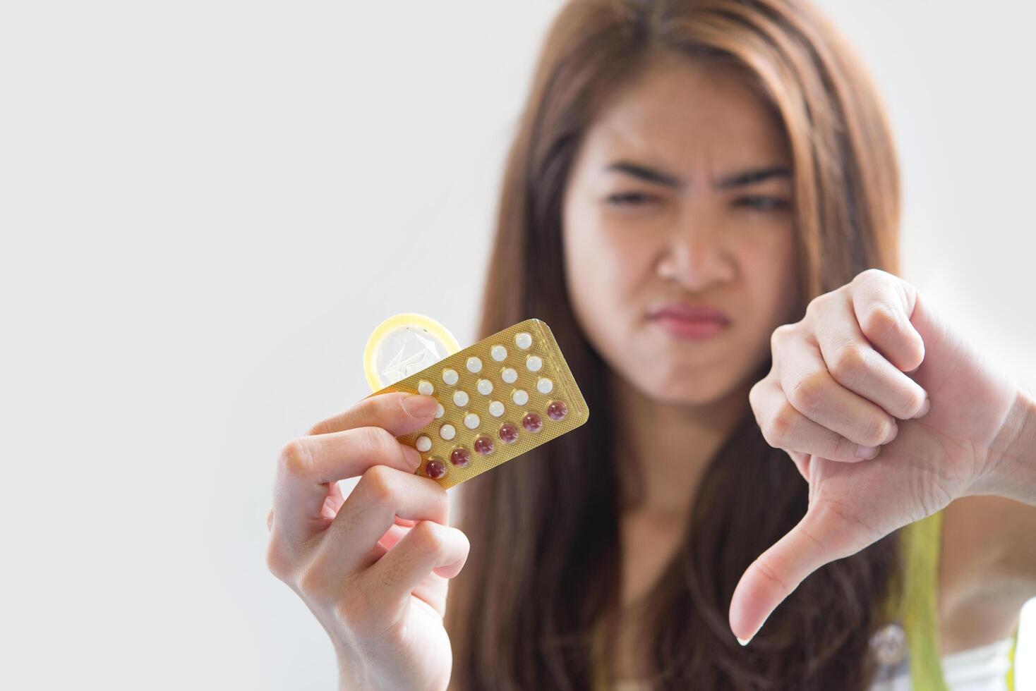 Mujer joven sosteniendo condones y píldoras anticonceptivas previenen el embarazo foto