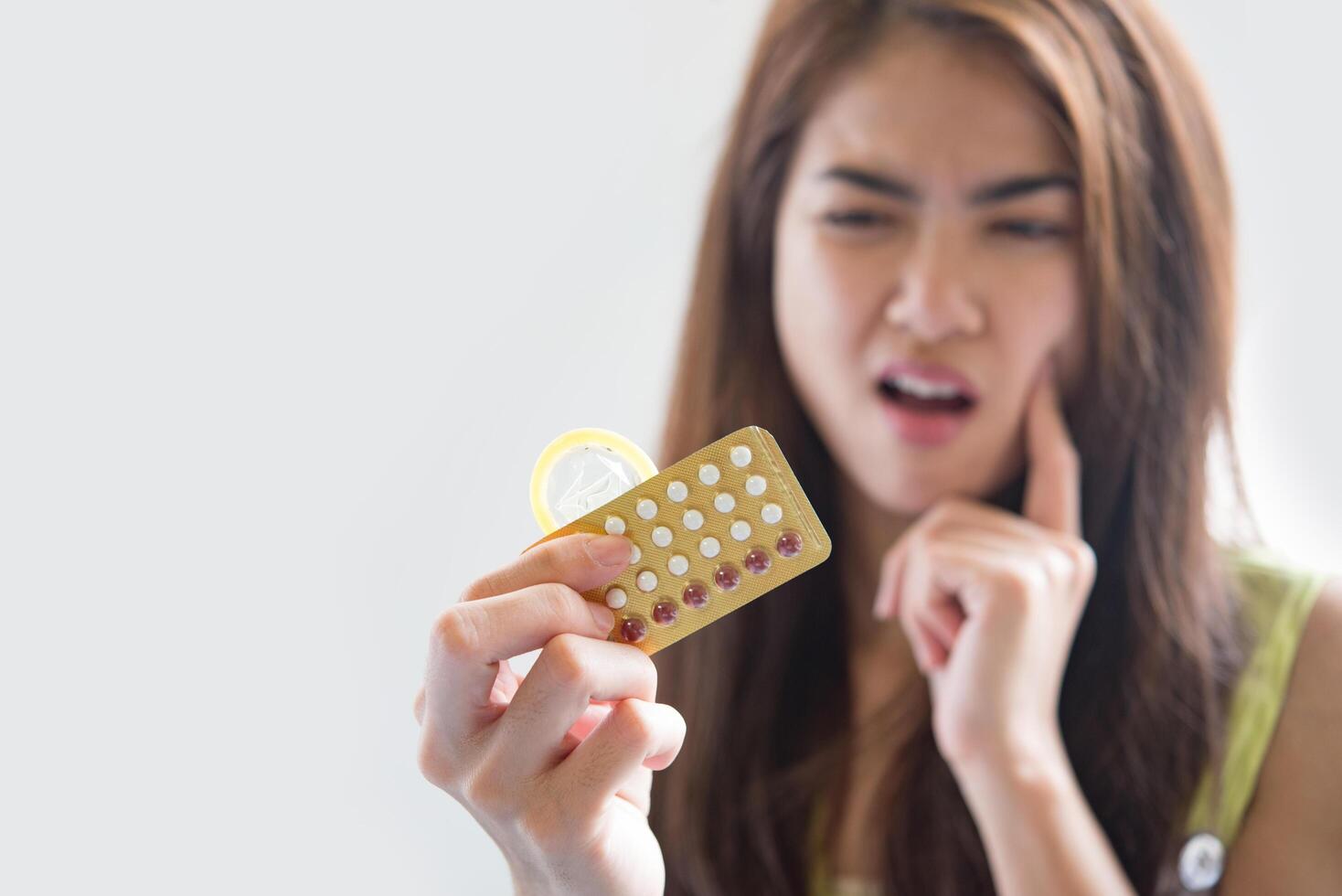 Mujer joven sosteniendo condones y píldoras anticonceptivas previenen el embarazo foto