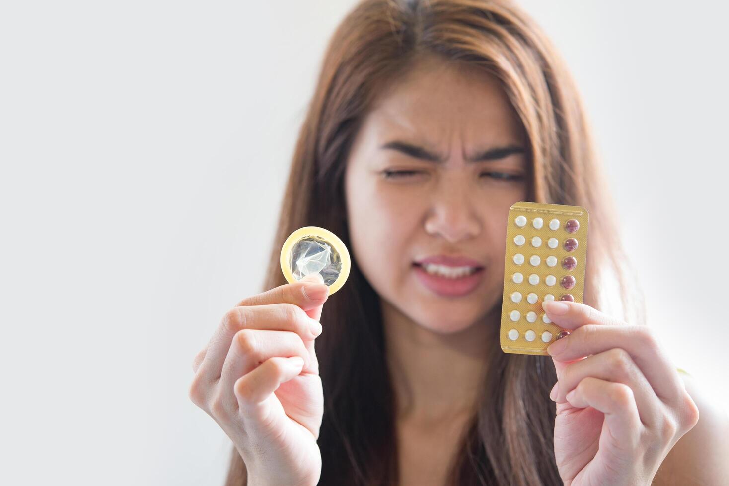 Mujer joven sosteniendo condones y píldoras anticonceptivas previenen el embarazo foto