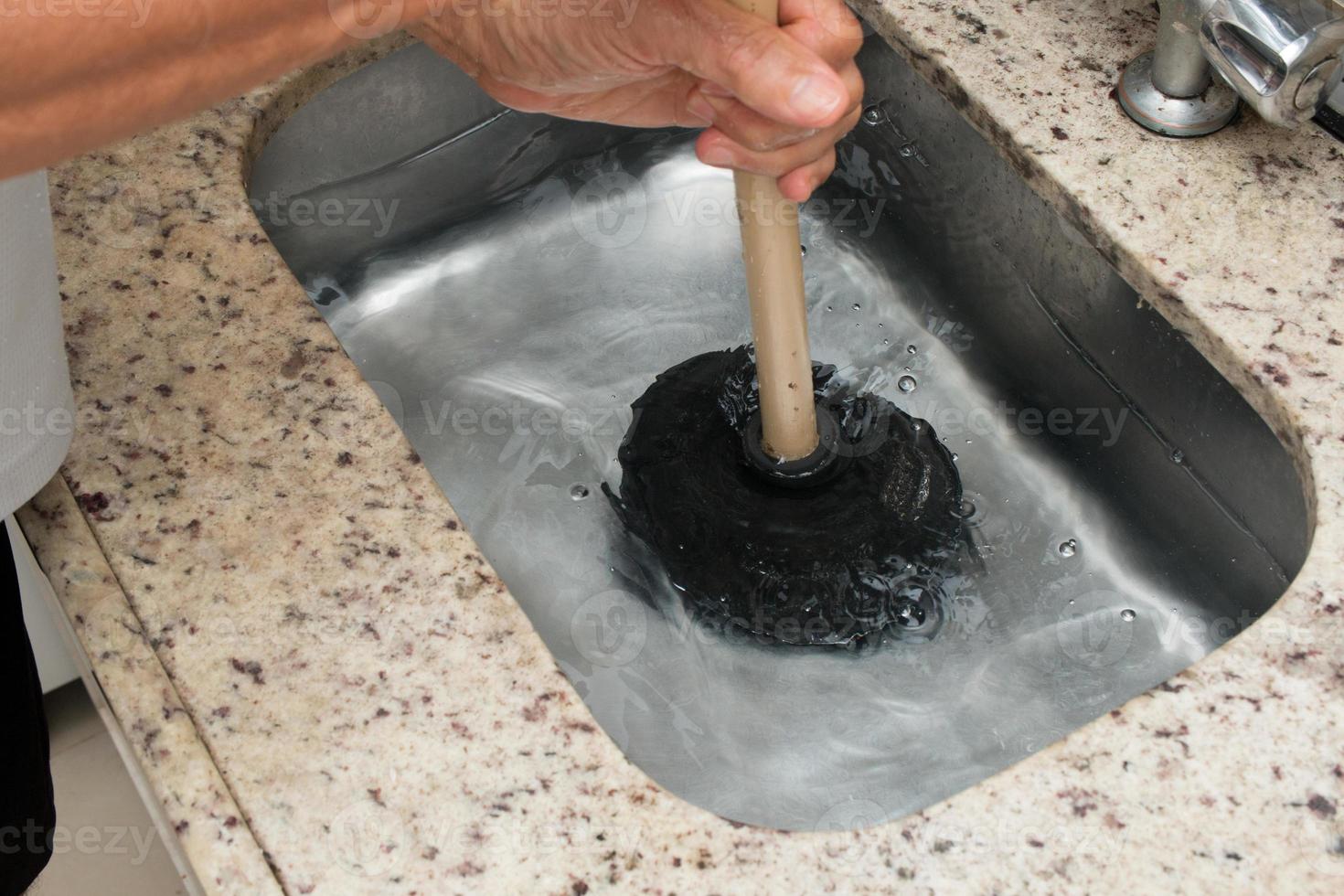 Man Using a Plunger to unstop his kitchen sink photo