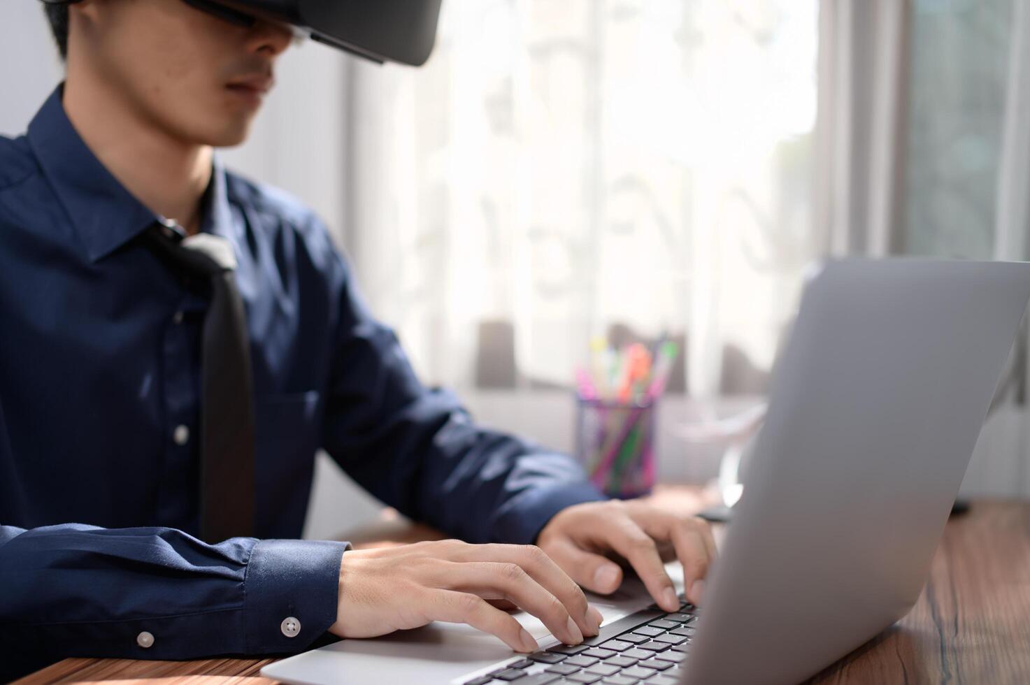 A man wearing a virtual reality headset is typing on a laptop photo
