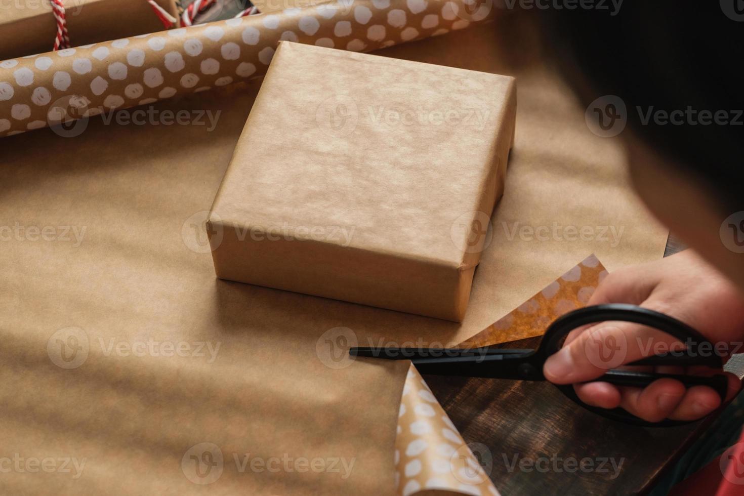 Cerrar mujer mano cortando papel kraft para envolver la caja de regalo de navidad en la mesa de madera foto