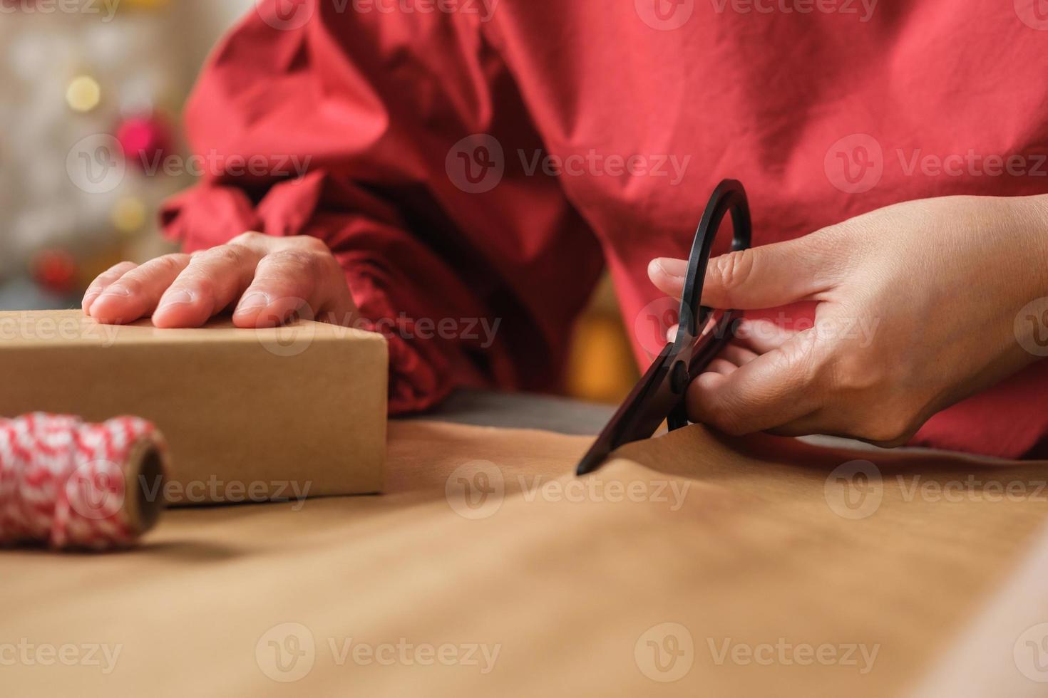 Cerrar mujer mano cortando papel kraft para envolver la caja de regalo de navidad en la mesa de madera foto