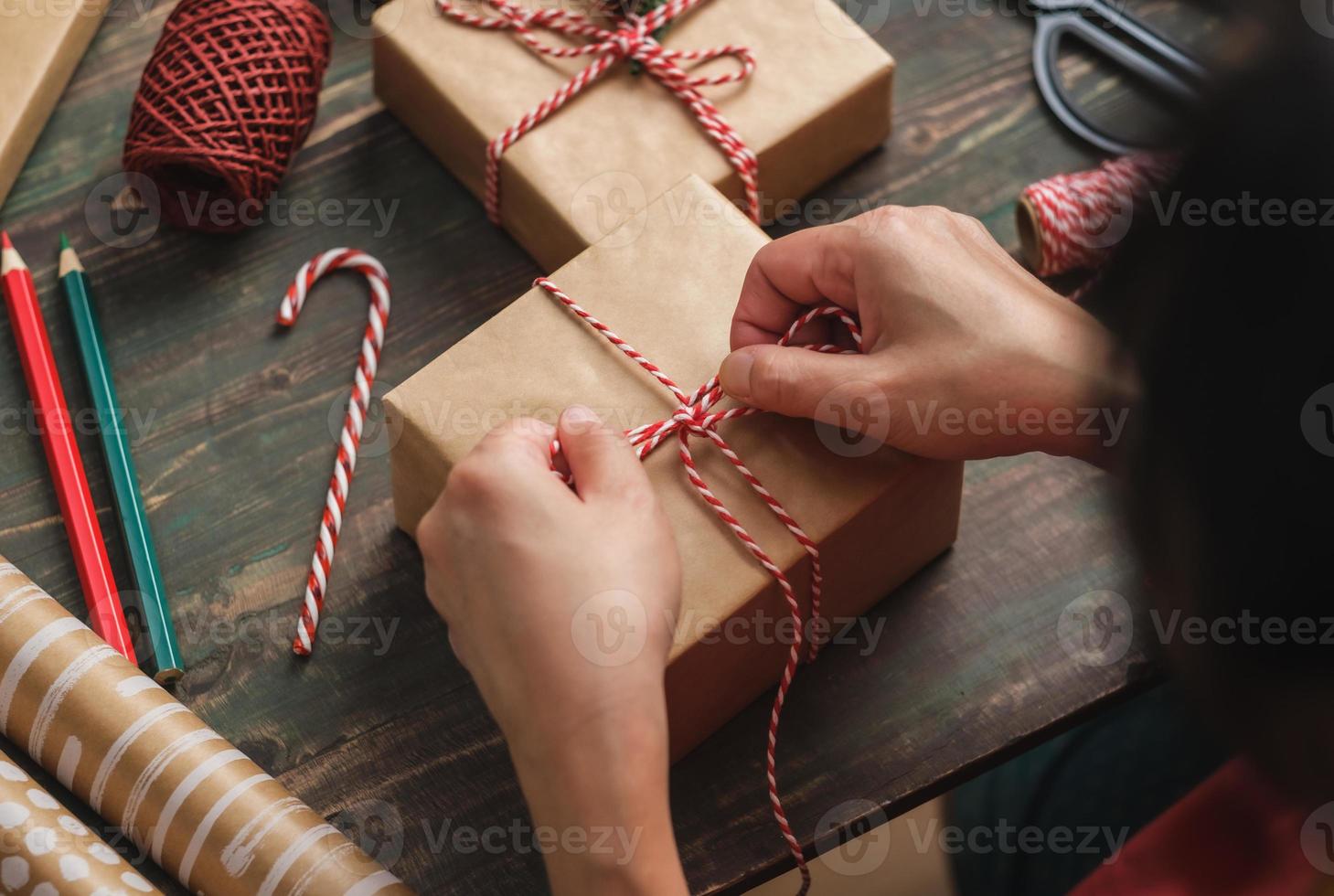 woman making Christmas handmade gift box with brown paper warpping with xmas decor on wood table photo