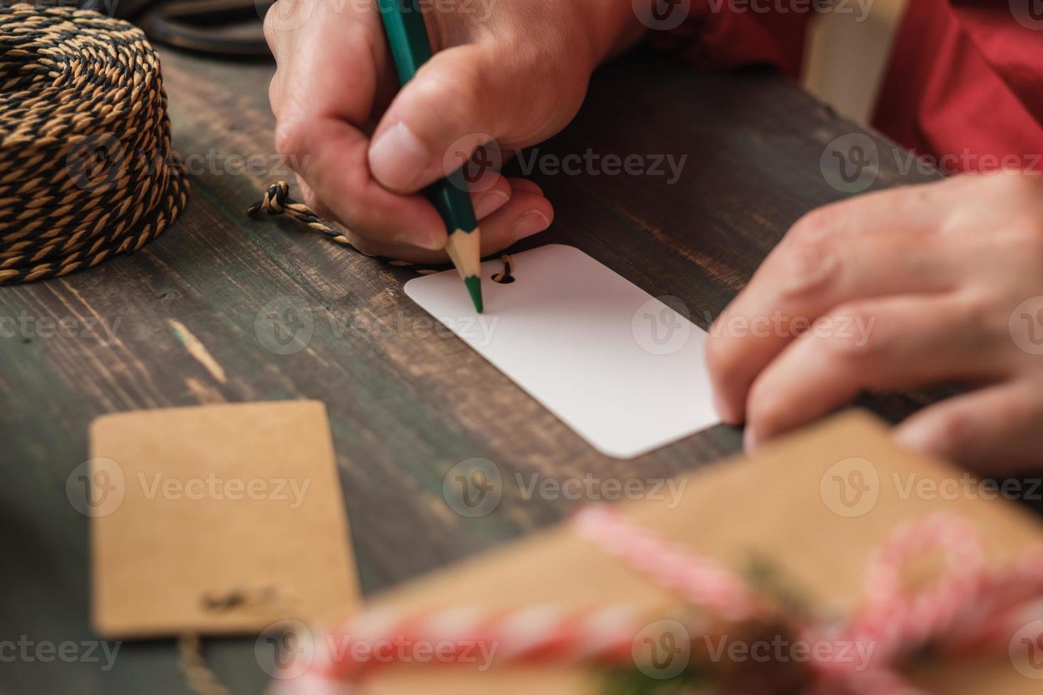 Mujer escribiendo etiqueta de regalo y adjuntar al regalo de Navidad en la mesa de madera foto