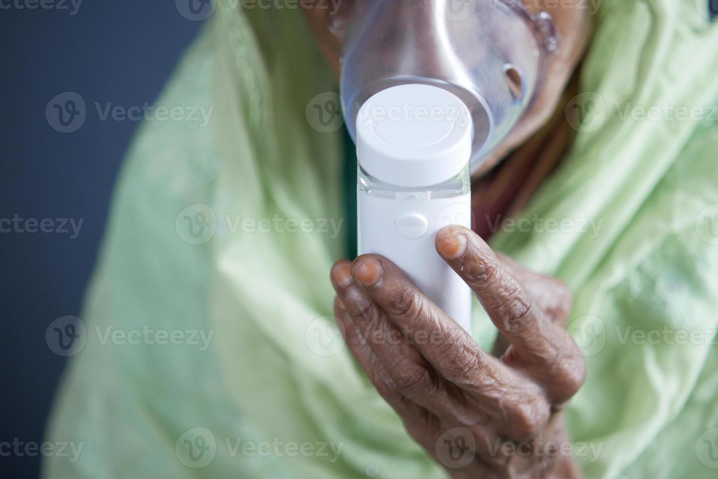 La mano de las mujeres mayores sostiene un nebulizador contra un fondo gris claro foto