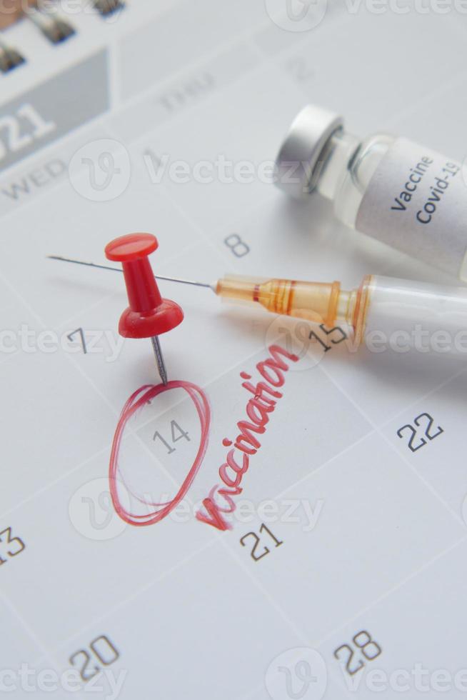 Concepto del día de la vacuna ampolla de vidrio con vacuna y jeringa en el calendario foto