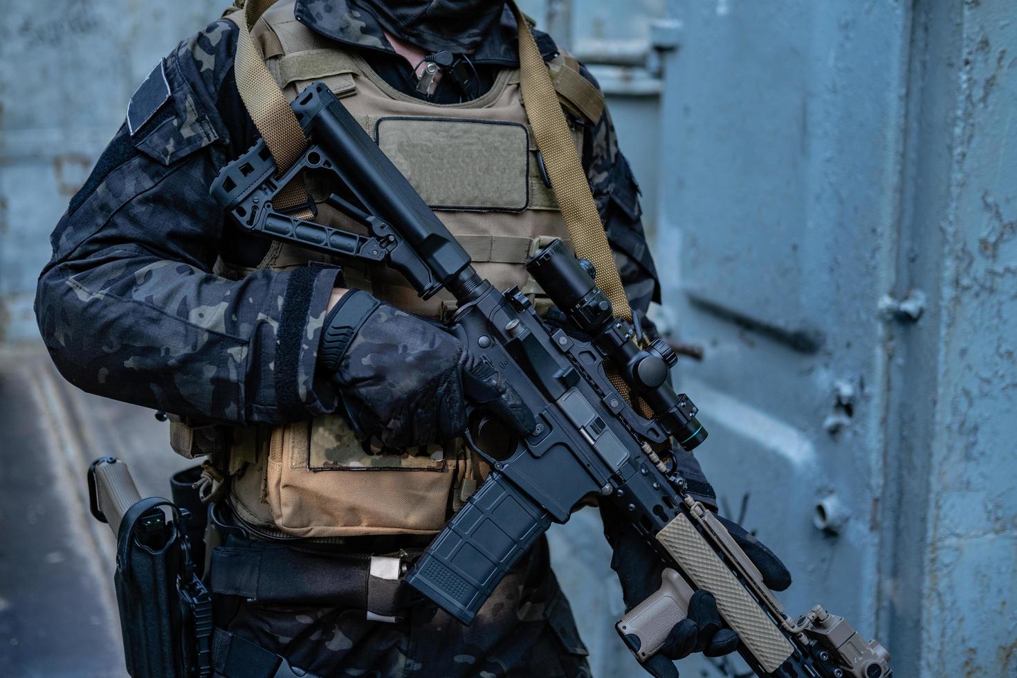 Soldado moderno en uniforme negro multicámara con rifle, fondo urbano foto