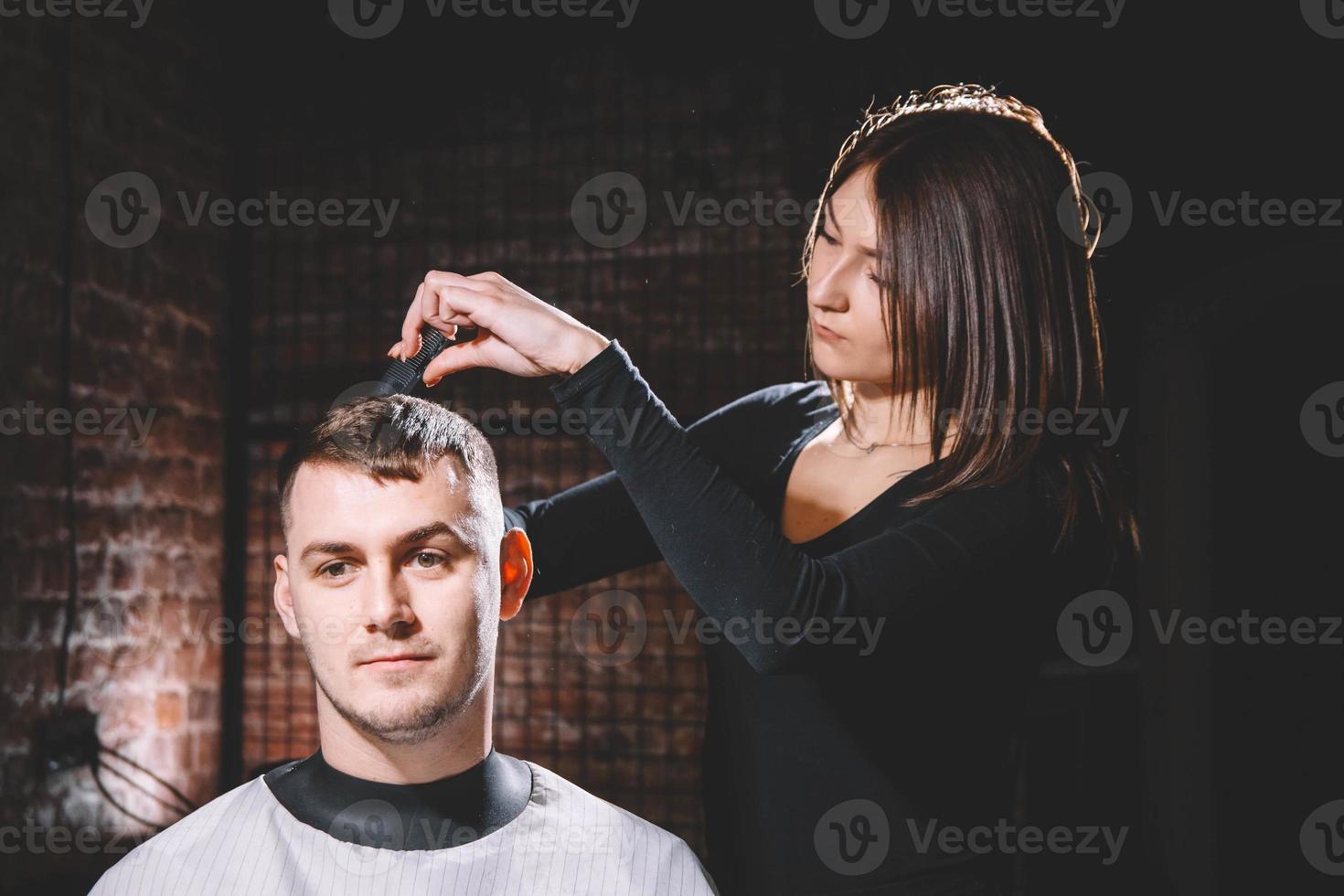 Beautiful female hairdresser cutting client's hair with scissors in a barber shop photo