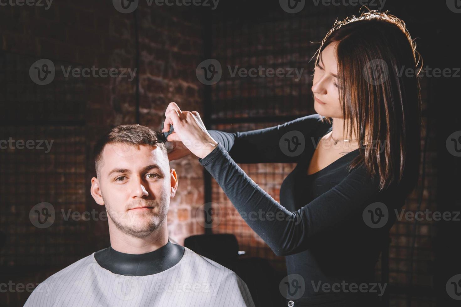 Hermosa peluquera cortando el cabello del cliente con unas tijeras en una peluquería foto