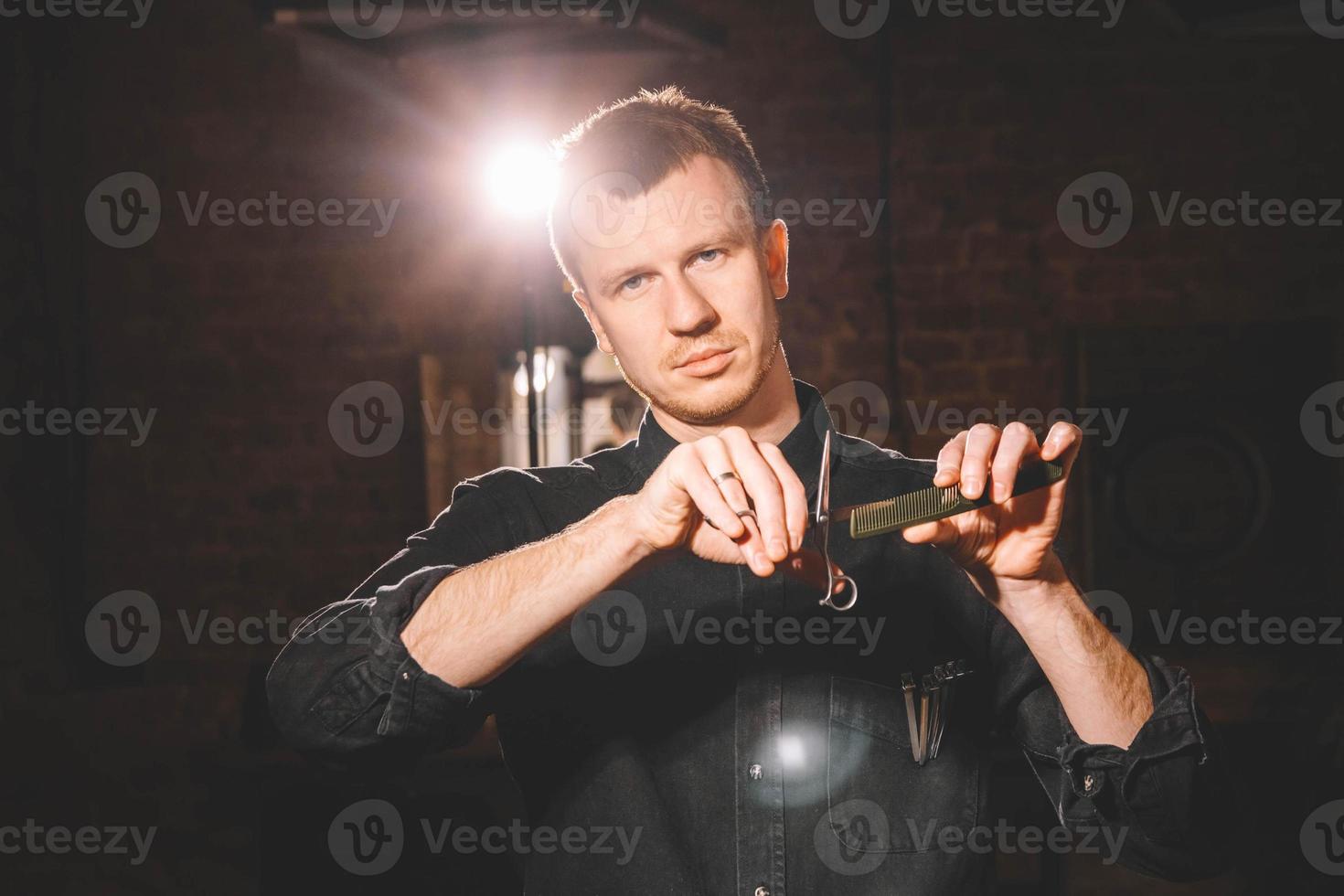 Barber is holding scissors and comb in his hands barbershop on a dark background photo