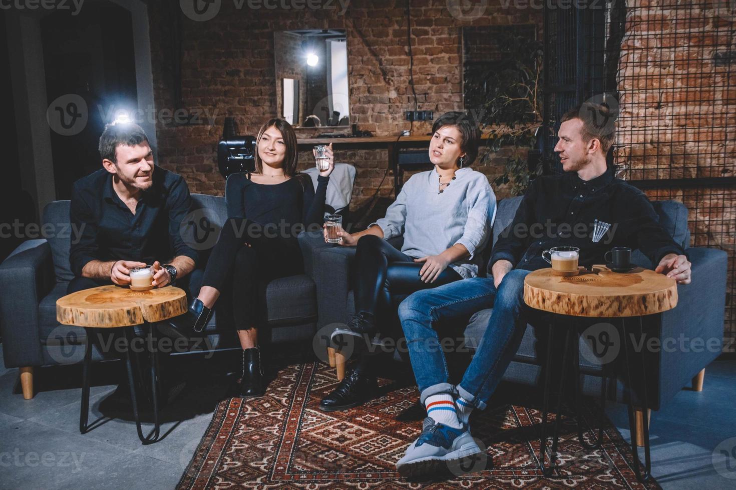 Cheerful guys and girls are sitting on sofa with cups in hands photo