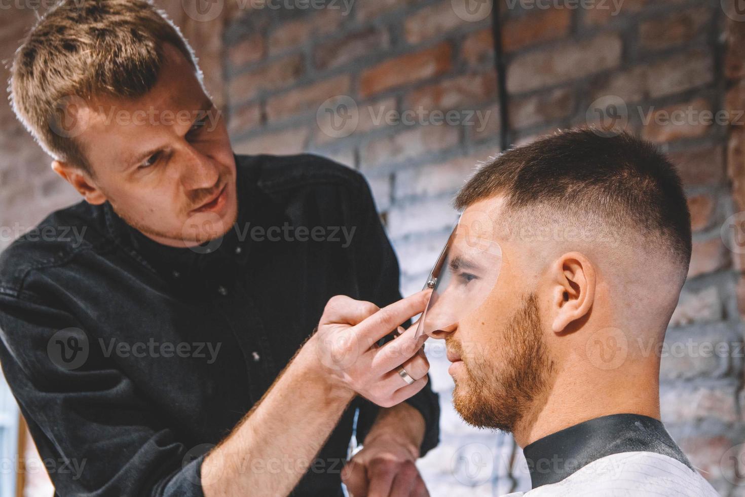 Macho joven peluquero cortando el cabello del cliente con unas tijeras foto