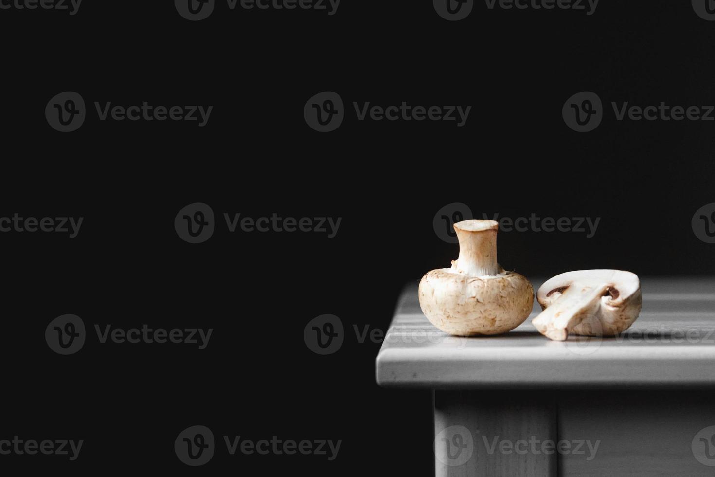 Mushrooms champignons lie in a row on a white table on a dark background photo