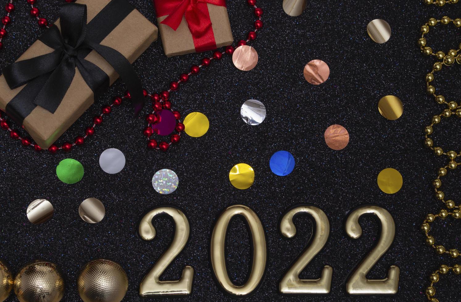 New Year 2022. Top view New Year mockup on black shiny background red ribbon, gift box, gold numbers and multicolored sparkles. Layout of postcards, photo