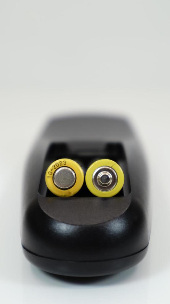 Black remote control with yellow AAA batteries on a white background. Battery replacement, spare parts. Remote control battery compartment close-up. Vertical photography photo