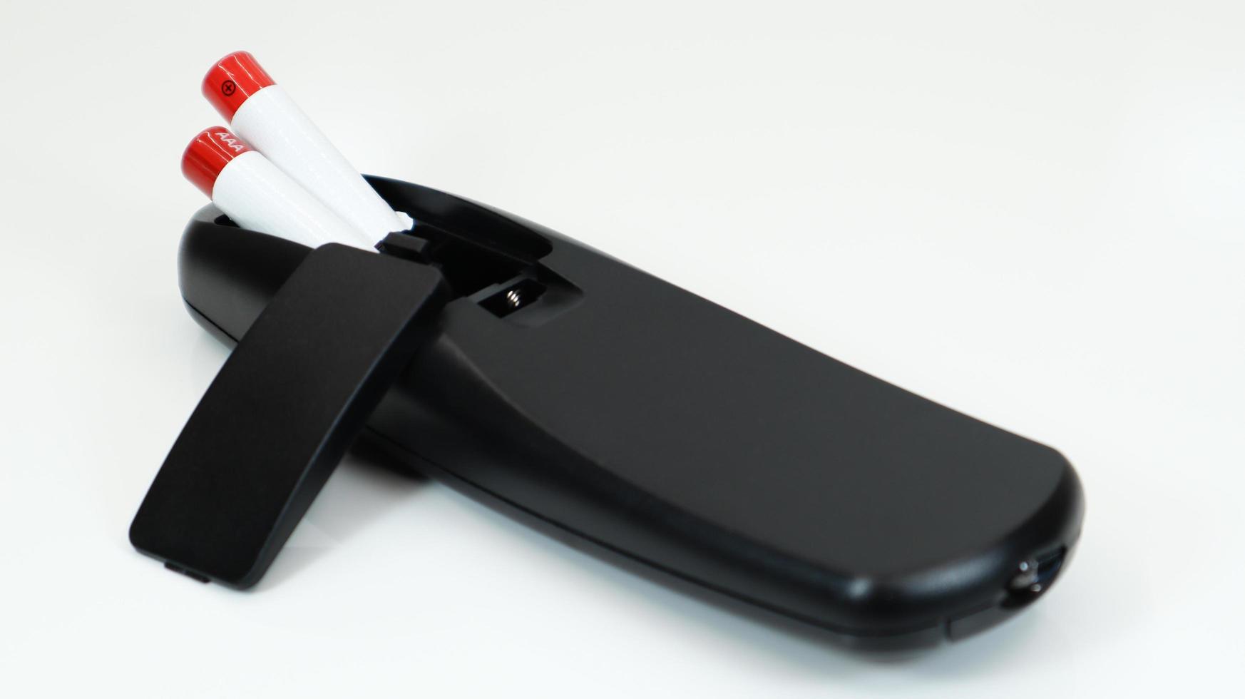 Black TV remote control with AAA alkaline batteries on a white background. Battery replacement, spare parts. Close up of the battery compartment of the remote control. photo