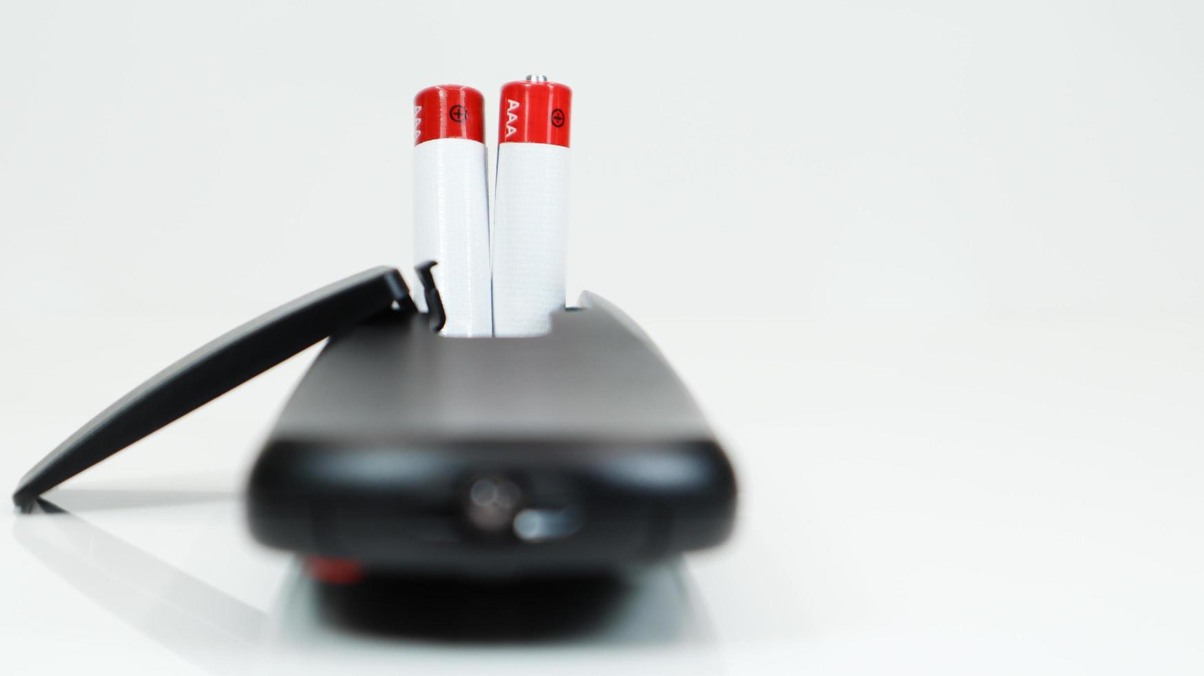Black TV remote control with AAA alkaline batteries on a white background. Battery replacement, spare parts. Close up of the battery compartment of the remote control. photo