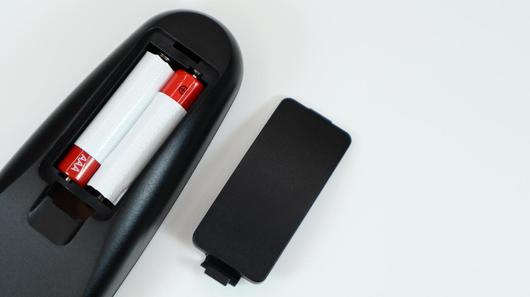 Black TV remote control with AAA alkaline batteries in red and white on a white background. Battery replacement, spare parts. Remote control battery compartment close-up. Copy space. photo