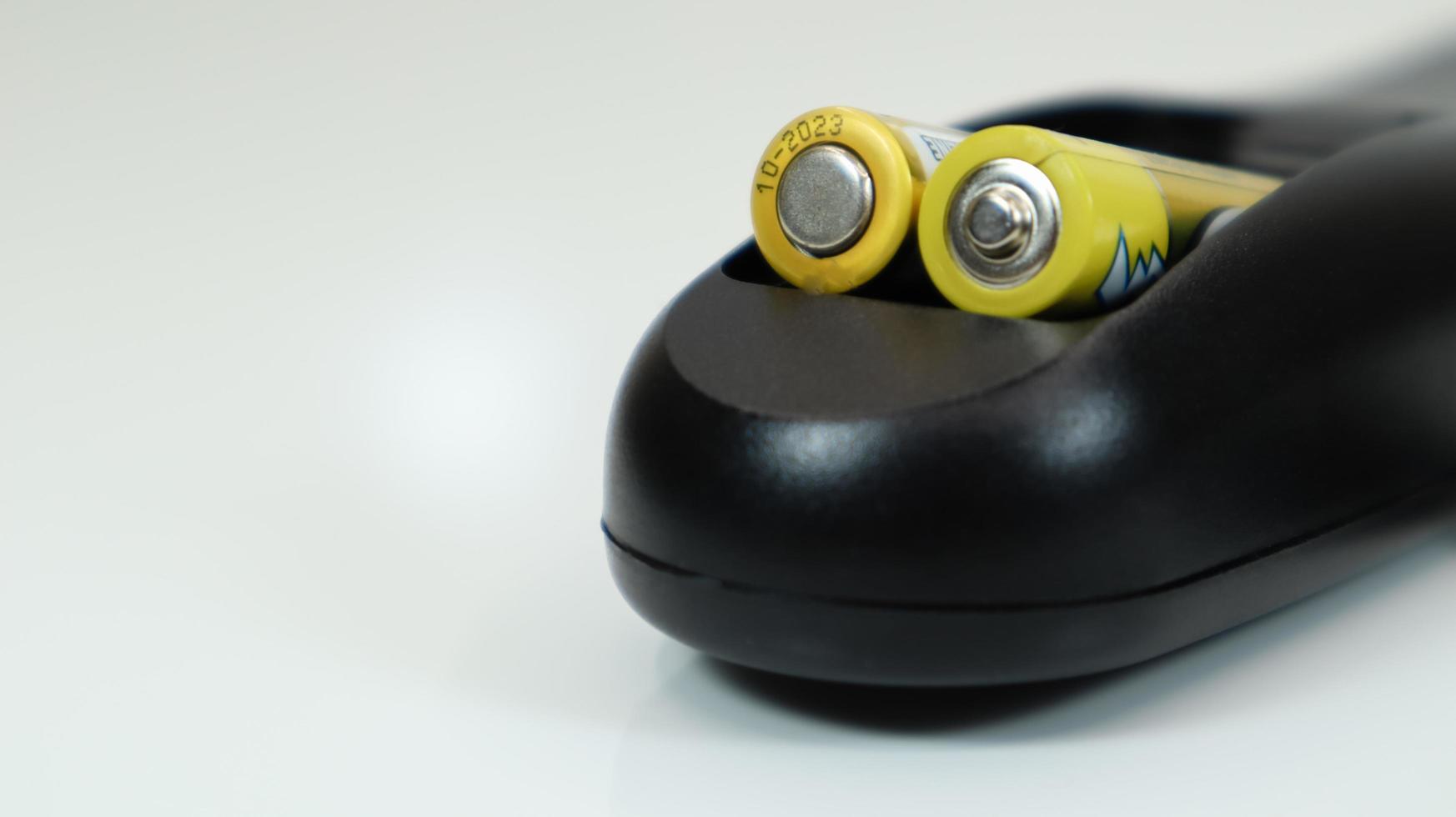 Black remote control with yellow AAA batteries on a white background. Battery replacement, spare parts. Remote control battery compartment close-up. Copy space photo