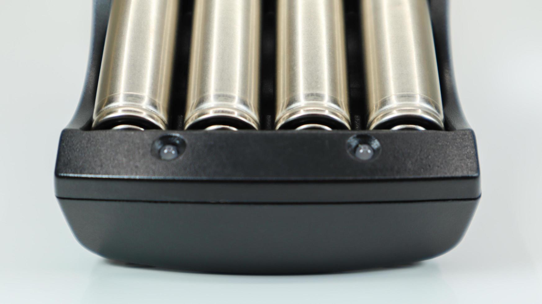 Rechargeable alkaline batteries in a battery charger on a white background. AA fast charger in black. The battery is charging. photo